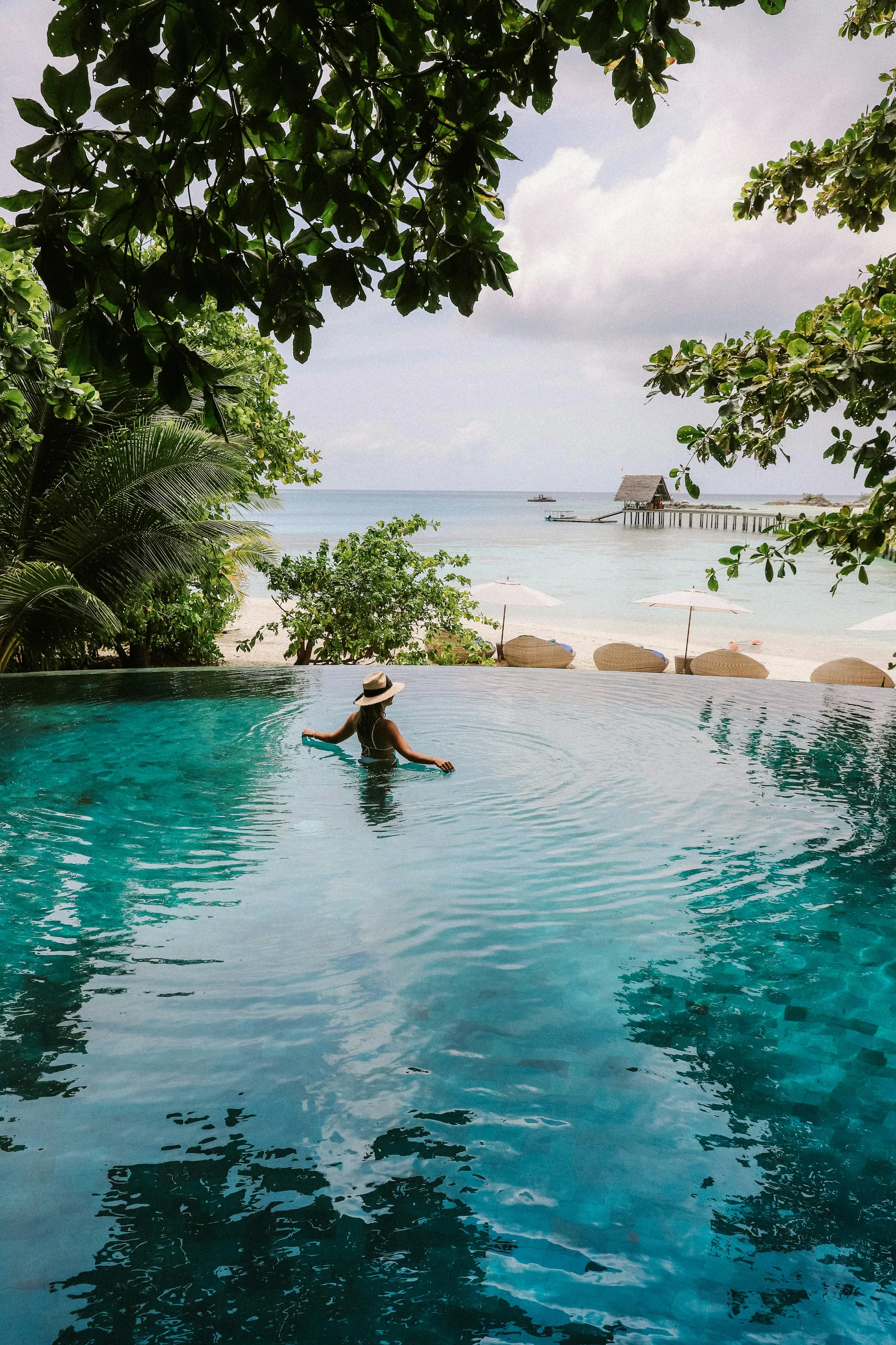 A guest relaxing in an infinity pool overlooking a tropical beach and the sea.