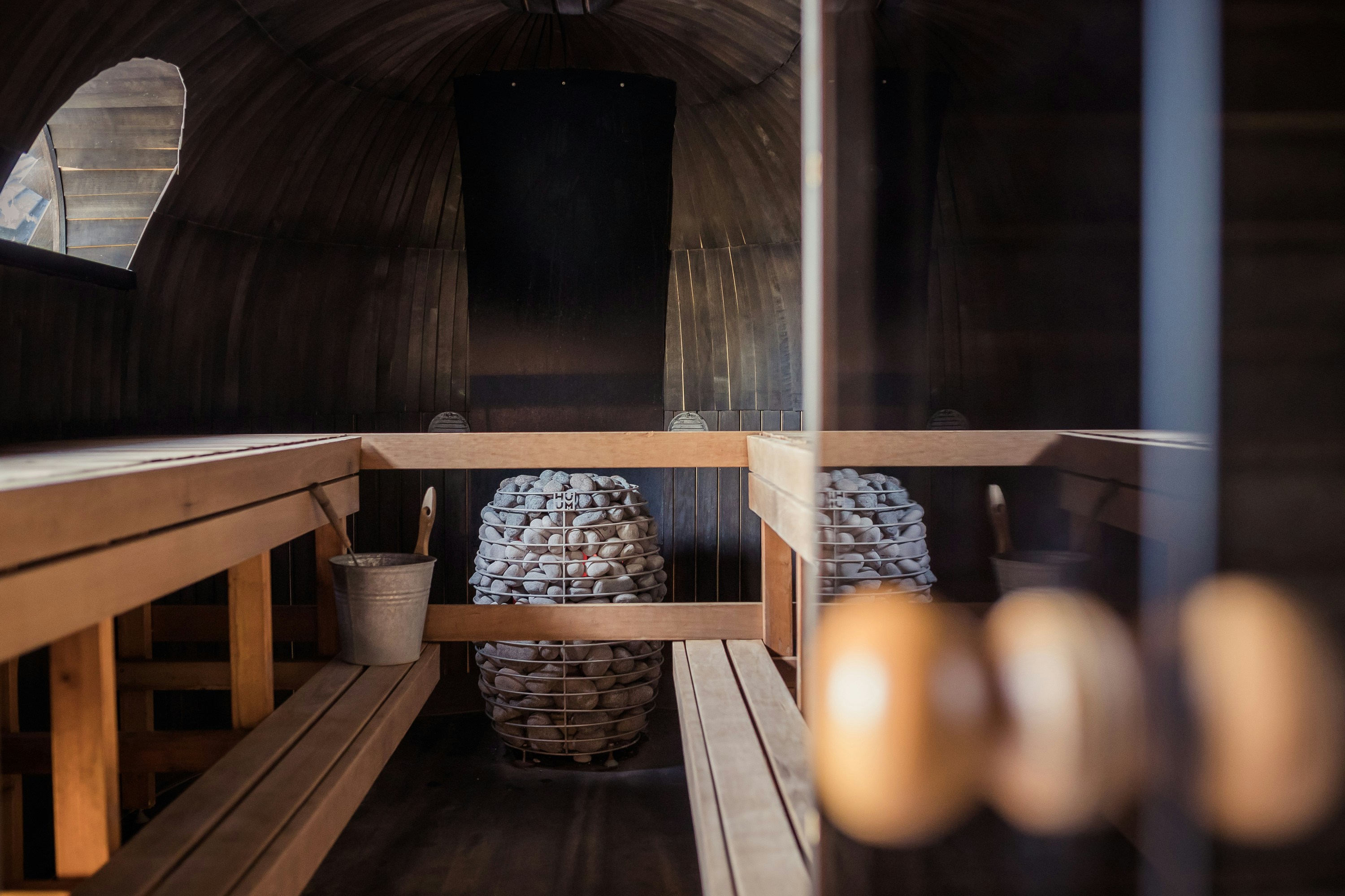 A wooden sauna with a stone-filled heater and warm natural light.